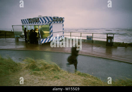 The Netherlands. Katwijk. North Sea. Boulevard with snackshop. Woman walking in wind and rain. Stock Photo