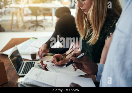 Two focused coworkers discussing notes while working together in a modern office with colleagues in the background Stock Photo