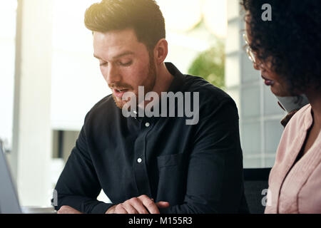 Two focused young work collegues talking business together while sitting at a table in a modern office Stock Photo