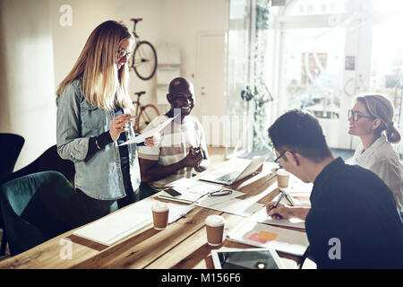 Young woman giving a presentation to smiling workers sitting together around a table in a modern office Stock Photo