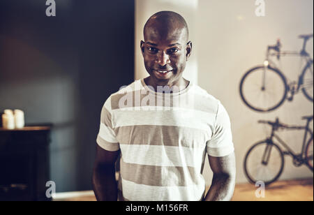 Casually dressed young African man smiling while standing alone in a creative modern office Stock Photo