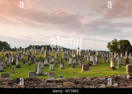 rural graveyard filled with old grave stones set on picturesque hill behind fieldstone wall Stock Photo