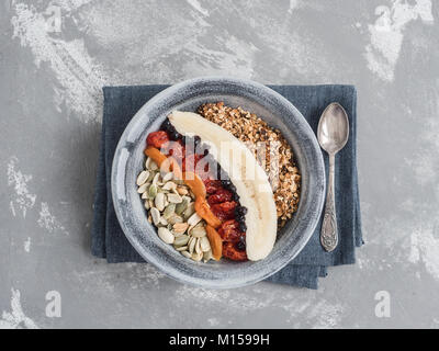 Muesli with banana, blueberries, dried apricots, carnelian cherry, peanuts and pumpkin seeds, in an old plate on a gray table Stock Photo