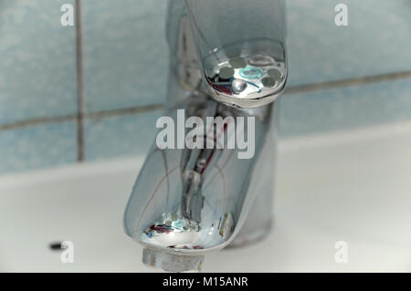 Shiny bath faucet , reflective mixing tap, with interesting reflections, mounted on a sink with tiles as background Stock Photo