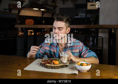 Funny hungry person eats pancakes on the breakfast. Young man sits at the table in the stylish home kitchen. The meal close to over. Stock Photo