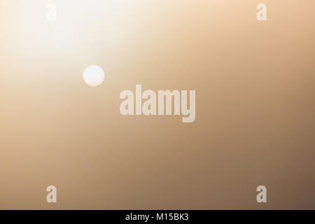 Misty morning sky covered by fog after raining during winter season with small sun shining sunlight through the fog making warm orange color on sky. Stock Photo
