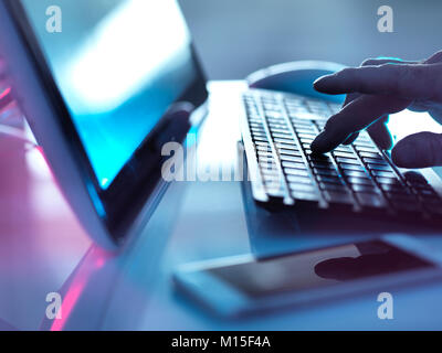 MODEL RELEASED. Computer use. Man working at PC with a mobile phone on the desk. Stock Photo