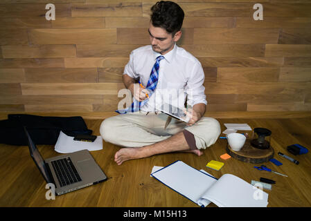 Remote working, thinking about a solution. Young man working at home in funny clothes. A barefoot businessman sits on the floor Stock Photo