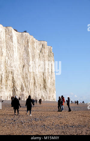 Tall white chalk cliff face with a sandy pebble beach at the bottom of the cliff lots of people are walking on the beach under the cliff, Seven Sister Stock Photo