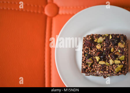 food photography of home made cake or biscuit made with natural ingredients of cranberry fruit pistachio nuts and cocao on a bright orange background Stock Photo