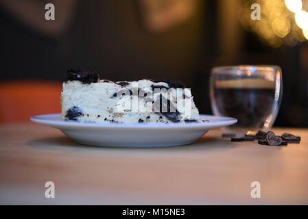 home made food of chocolate biscuit cheesecake with wooden love heart decorations and lighting with a hot drink of expresso coffee in background Stock Photo