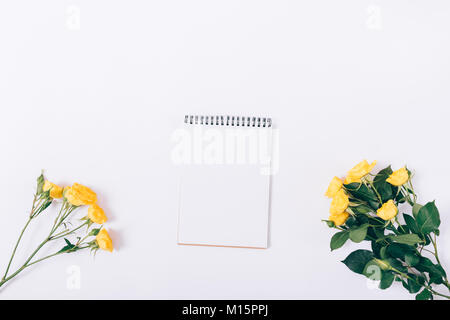 Paper notebook and bouquets of yellow roses on a white table top view Stock Photo