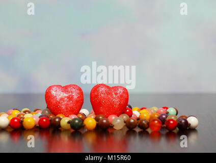 On wooden table are colorful beads and 2 red hearts. To the rear there is a place for a label. Stock Photo