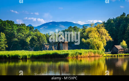 Dumbrava, Sibiu, Romania: Landscape of a lake with windmill in the golden light before sunset. Stock Photo