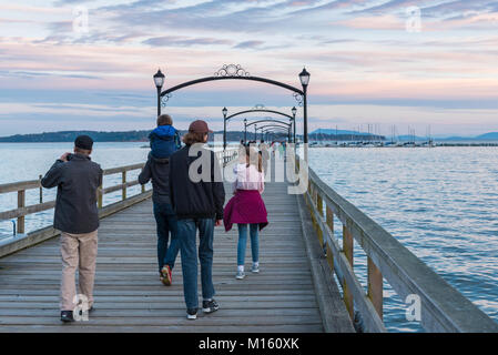 A family walks down the White Rock Pier at sunset. The pier, built in the 1920's, is a popular tourist attraction. Stock Photo