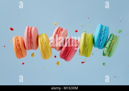 Different types of macaroons in motion falling on blue background. Sweet and colourful french macaroons falling or flying in motion. Stock Photo
