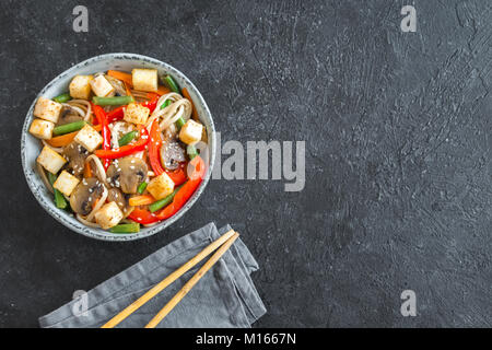 Stir fry with udon noodles, tofu, mushrooms and vegetables. Asian vegan vegetarian food, meal, stir fry over black background, copy space.