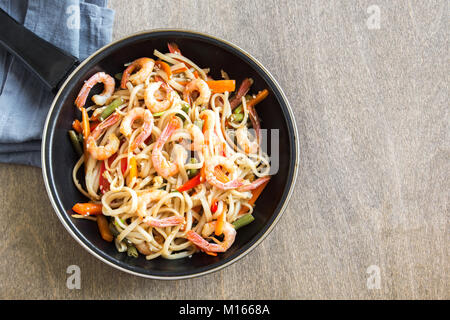 Stir fry with udon noodles, shrimps (prawns) and vegetables. Asian healthy food, meal, stir fry in wok over wooden background, copy space. Stock Photo
