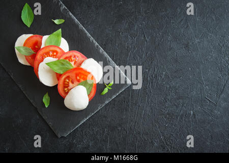 Traditional Italian Caprese Salad - sliced tomatoes, mozzarella cheese and basil on dark stone background, top view, copyspace. Caprese Salad, italian Stock Photo
