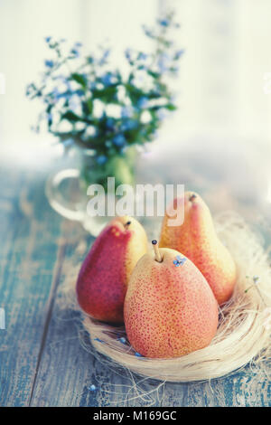 Beautiful ripe yellow pear lying on a wooden table in a lit room in a rustic style on the background of a bouquet of small blue forget-me-nots. Copy space. Stock Photo