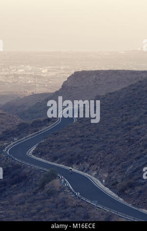 Alone cyclist on winding mountain road. Stock Photo