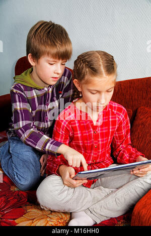 The boy teaches his sister to use the electronic tablet Stock Photo