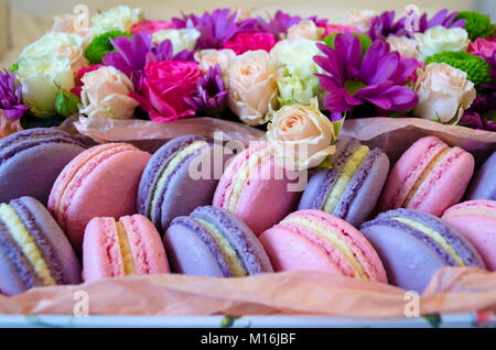 French macaroon cake. Violet and pink macaroons in a box with flowers on the bed. Stock Photo