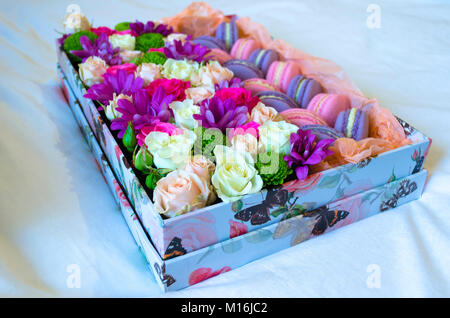 French macaroon cake. Violet and pink macaroons in a box with flowers on the bed. Stock Photo