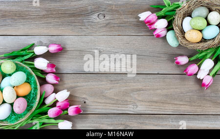 Traditional basket and bird nest filled with colorful eggs and pink tulips in both corners on weathered wooden boards for Easter background Stock Photo