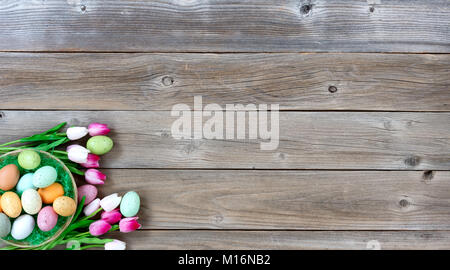 Basket filled with colorful eggs and pink tulips in lower left corner on weathered wooden boards for Easter background Stock Photo