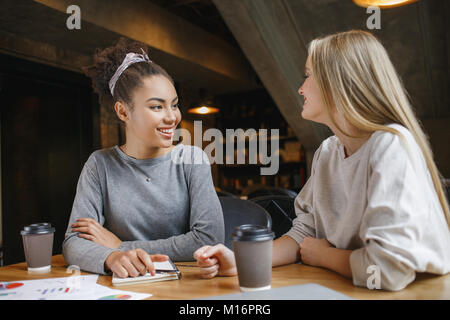 Young women students having a business lunch drinking hot coffee doing project discussion looking at each other smiling joyful Stock Photo