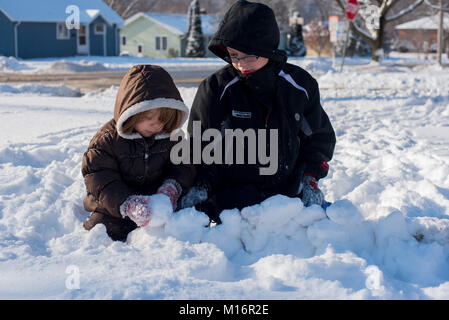 Two children wearing winter clothes play in the snow on a sunny day in the United States. Stock Photo