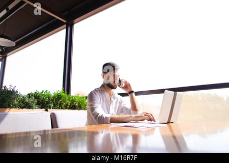 Prosperous sales manager reading documents, using laptop at tabl Stock Photo