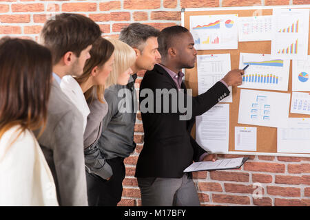 Business Colleague Looking At Graph Attached On Bulletin Board Over The Brick Wall Stock Photo