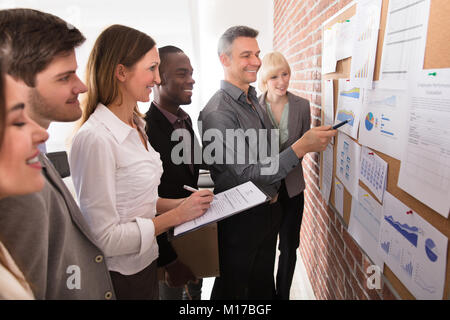 Mature Manager Analyzing The Graph With His Colleague Attached On Bulletin Board Stock Photo