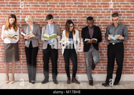Diverse Group Of Businesspeople Standing Near The Brick Wall Reading Books Stock Photo