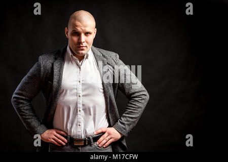 A  bald man businessman  in a white shirt, gray suit stands,  looks seriously and holds his hands at the waist on a black isolated background Stock Photo