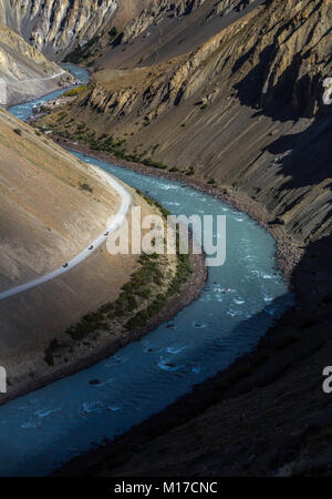 Bird's eye view of Spiti river and bikers riding the dirt road above that Stock Photo