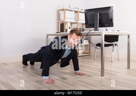 Young Businessman Doing Pushups On Hardwood Floor Stock Photo