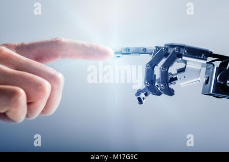 Close-up Of Businessperson's Finger Touching Robotic Finger On Blue Background Stock Photo