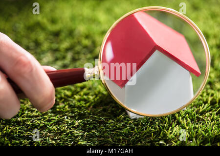 Close-up Of A Businessperson's Hand Looking At House Model Through Magnifying Glass Stock Photo