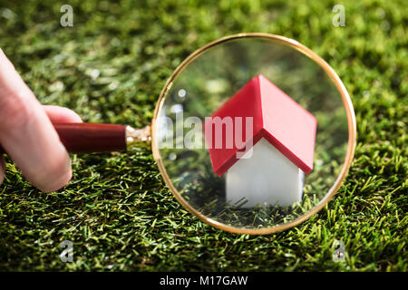 Close-up Of A Businessperson's Hand Looking At House Model Through Magnifying Glass Stock Photo