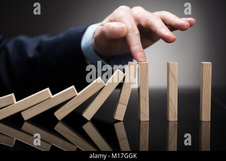 Close-up Of A Businessperson Stopping Wooden Blocks With His Finger From Falling On Desk Stock Photo