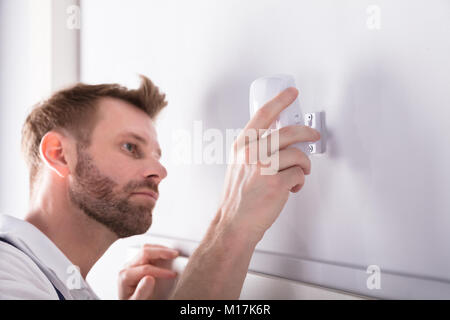 Close-up Of Young Male Electrician Installing Security System Door Sensor On Wall Stock Photo