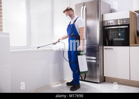 Young Man Spraying Pesticide On Windowsill In Kitchen Stock Photo