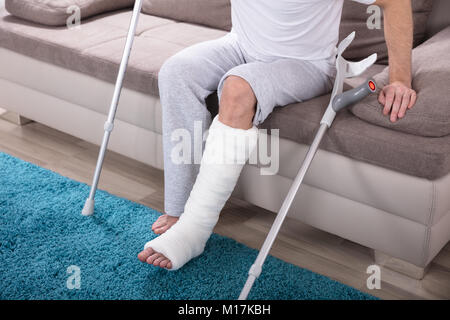Young Man With Broken Leg Using Crutches To Get Up From Sofa Stock Photo