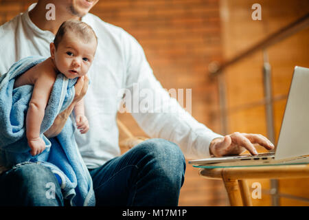 man working at desk at home with laptop, holding cute babys, looking at screen