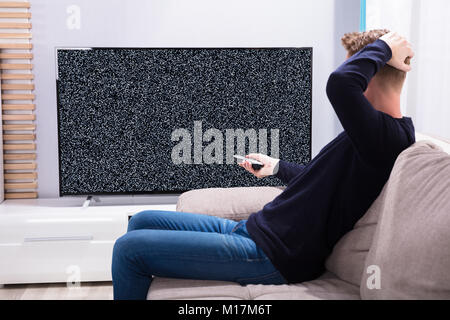 Man Sitting On Sofa Looking At Television With No Signal Stock Photo