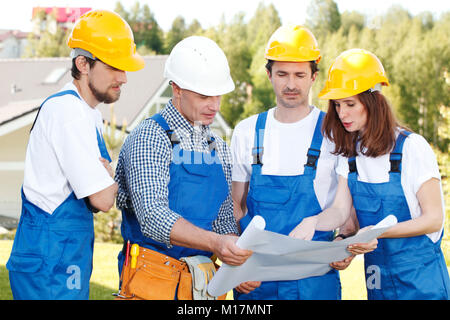 Team of Builders in hardhats with blueprint outdoors Stock Photo
