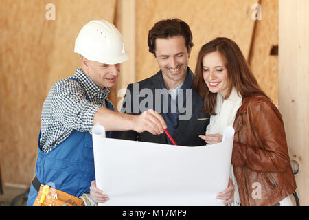 Worker shows house design plans to a young couple at construction site Stock Photo